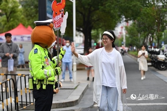 6月7日上午9時，隨著鈴聲的響起，2023年江西高考正式開考，江西省的53.57萬考生以縣（區(qū)）為單位隨機安排在全省256個考點、18968個考場參加高考。圖為“小熊交警”和考生擊掌鼓勵。 人民網(wǎng)記者 時雨攝