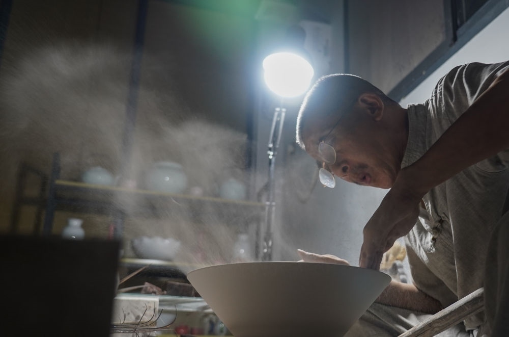 ↑ 在景德鎮(zhèn)，手工匠人吹去坯內(nèi)的泥土（2021年7月14日攝）。