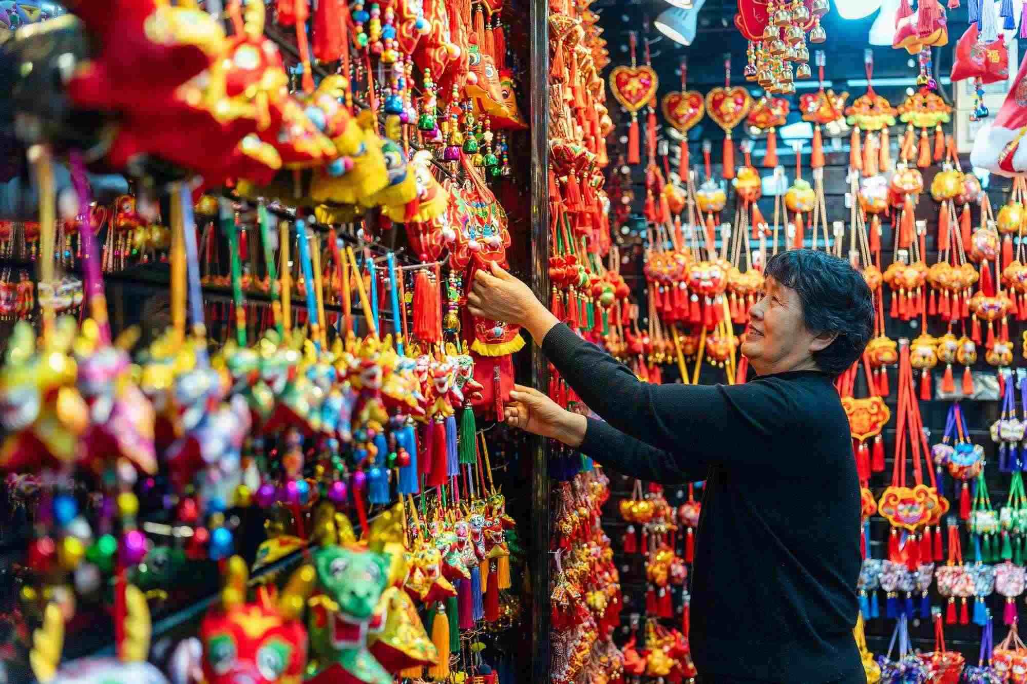 2023年12月11日，金華義烏國(guó)際商貿(mào)城，龍年喜慶用品掛滿攤位，顧客正在挑選中。