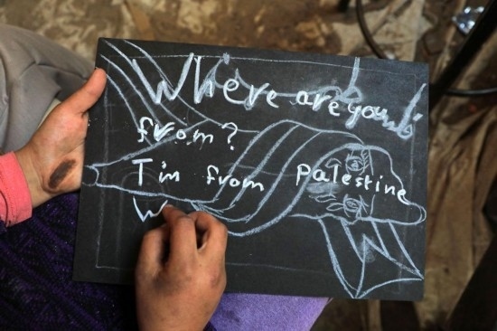 2023年12月28日，一名學(xué)生在加沙地帶南部城市拉法一所學(xué)校的臨時(shí)教室中寫下“我來自巴勒斯坦”的字樣。新華社發(fā)（里澤克·阿卜杜勒賈瓦德攝）