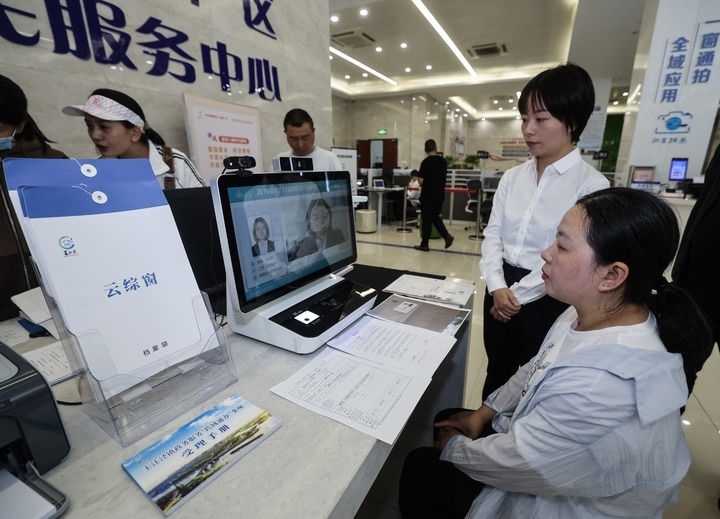 在浙江省嘉興市秀洲區(qū)王江涇鎮(zhèn)便民服務中心的“跨域通辦·云綜窗”窗口，辦理開業(yè)登記的個體工商戶（右一）通過該系統(tǒng)與江蘇省蘇州市吳江區(qū)盛澤鎮(zhèn)行政審批局工作人員視頻連線，進行身份讀取及材料線上審核（2024年5月9日攝）。新華社記者 徐昱 攝