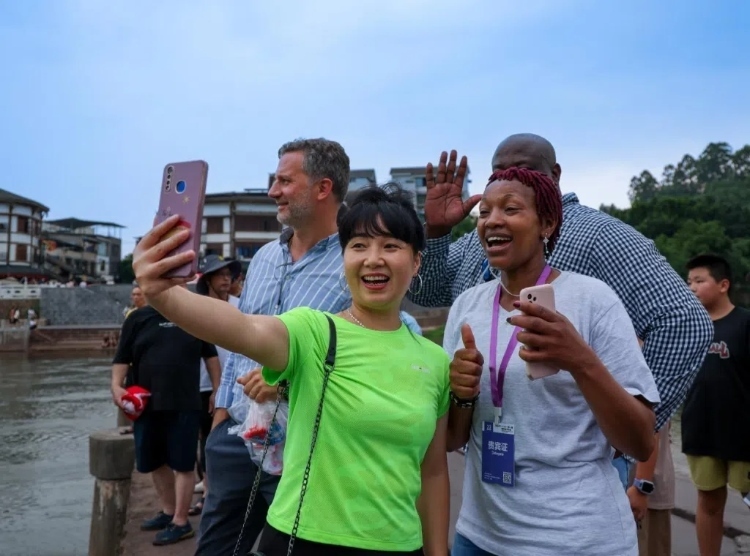 2024“一帶一路”媒體合作論壇聯(lián)合采訪調(diào)研行成員在樂(lè)山蘇稽古鎮(zhèn)與游客合影留念。本報(bào)記者 伊霄攝