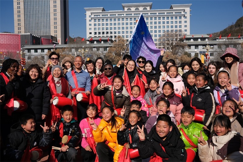 中外青年學子在安塞文化廣場觀看陜北腰鼓和大秧歌表演后合影留念，大家踏著鼓點共舞，翻飛的紅綢與躍動的身影交織，在黃土地廣場上繪出一幅生動的陜北民俗互動畫卷